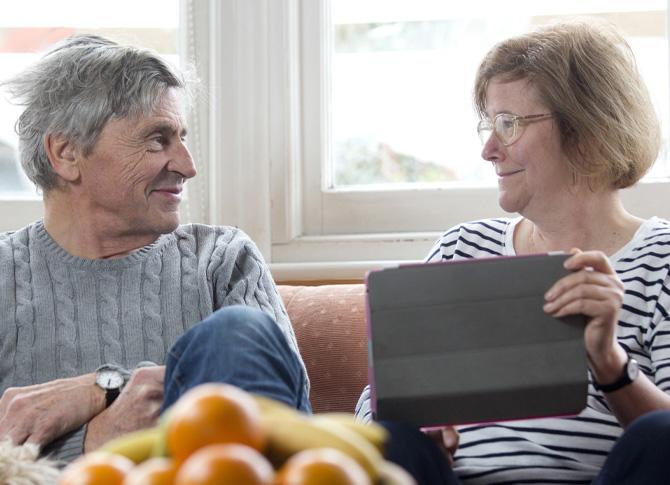 A man and woman smile at each other while holding an iPad